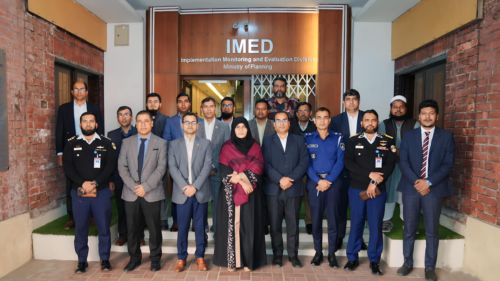 Training participants and staff pose together beneath the IMED signage after a completed session.