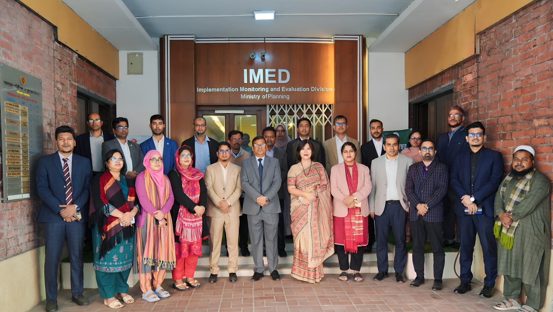 Group photo of training participants beneath the IMED signage, with a woman in a teal saree standing in the front row.
