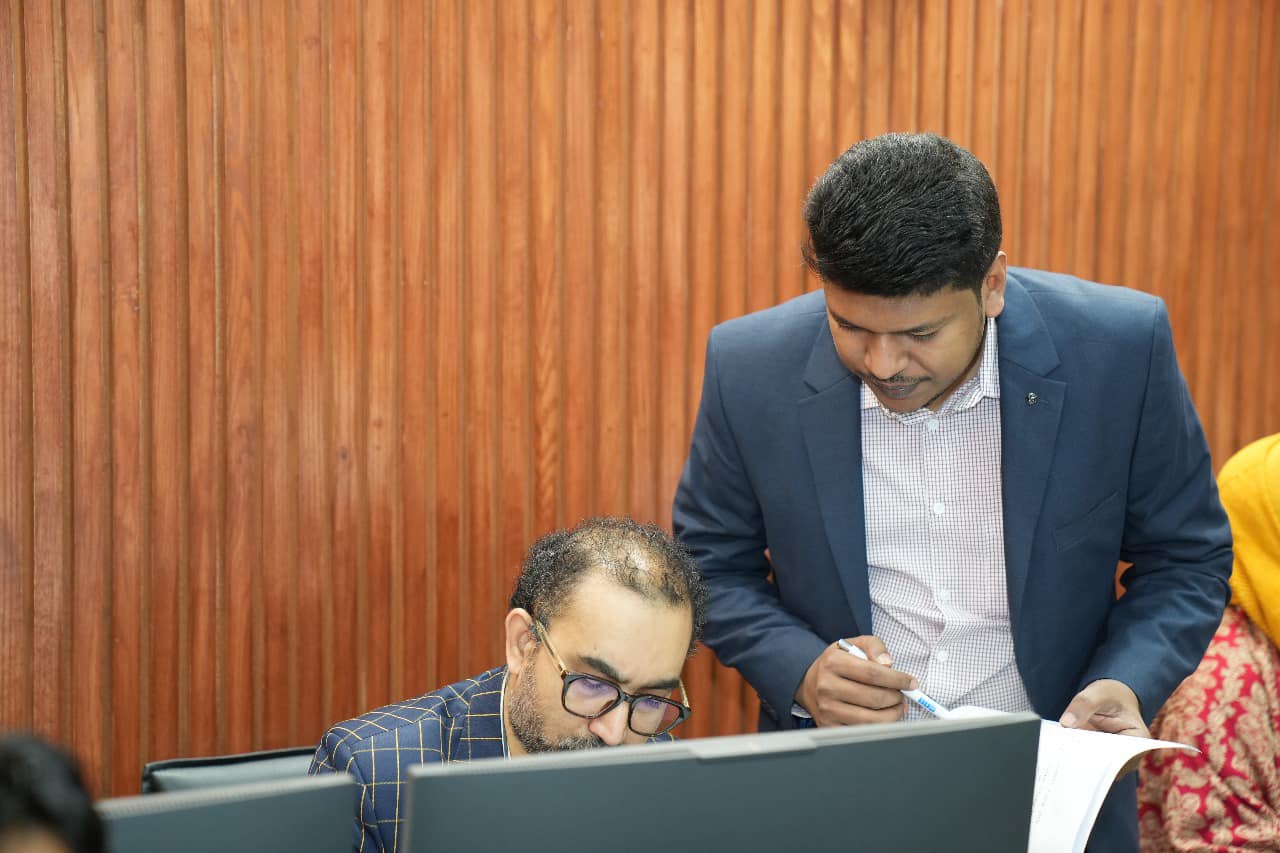 Raihan Khan helps a seated participant navigate the e-PMIS system on his computer during the session.