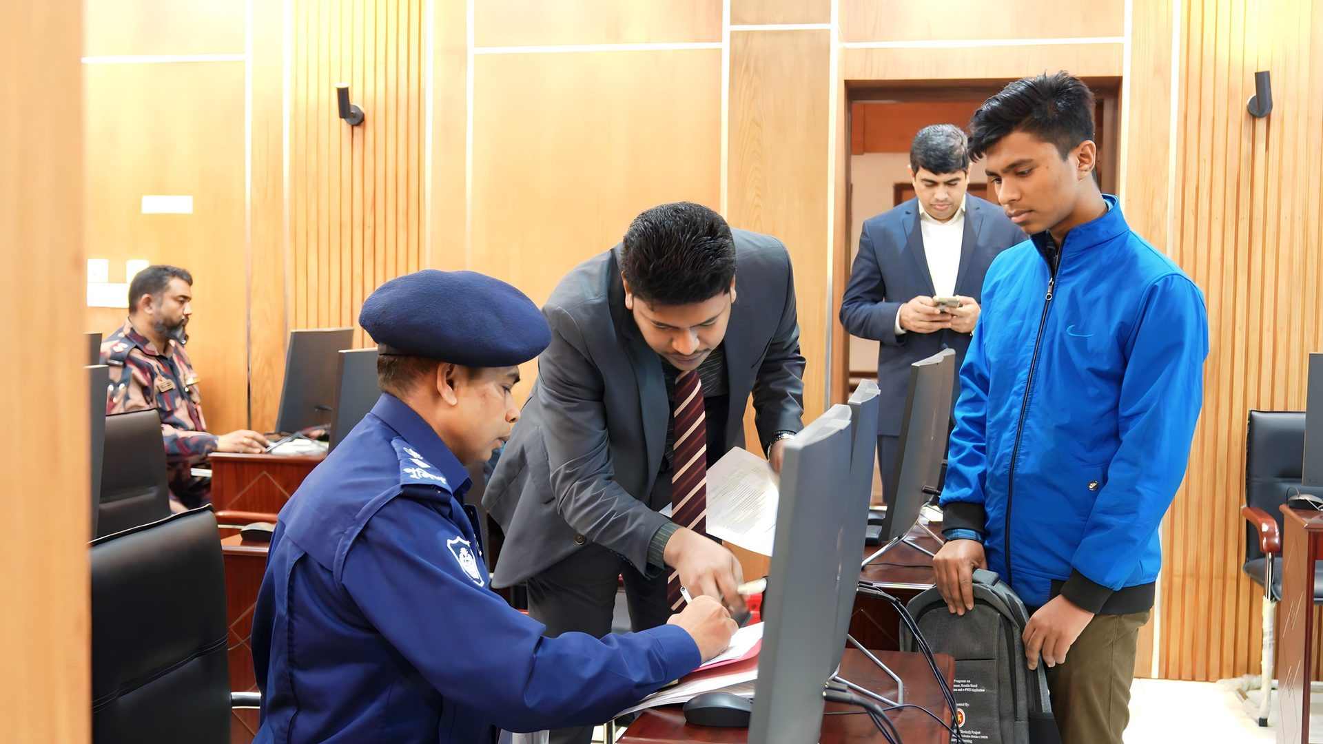 A police officer signs a registration form at the front desk while Raihan Khan assists during check-in.