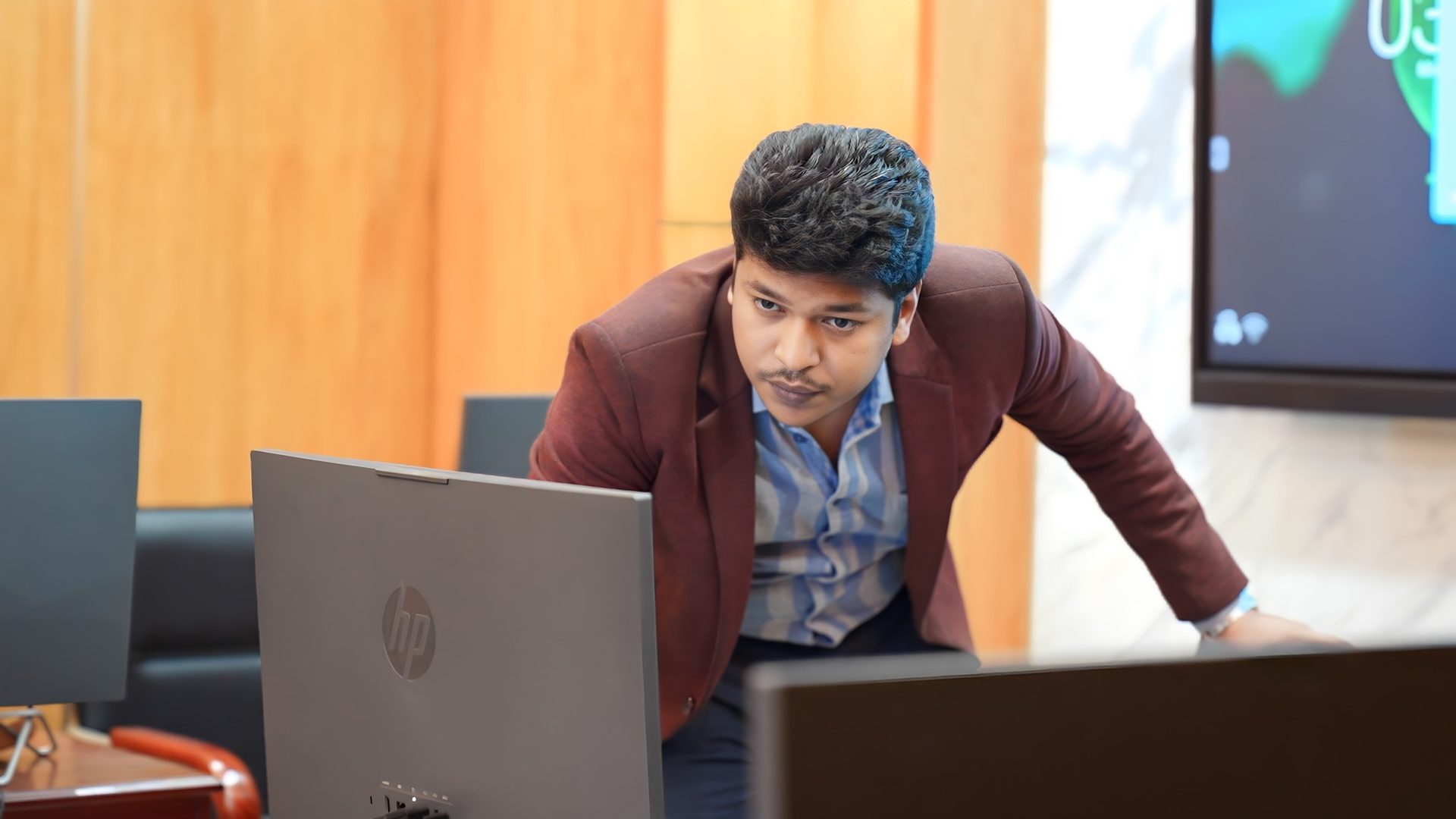 Raihan Khan in a maroon blazer reviews a data dashboard displayed on a large wall-mounted screen during the training session.
