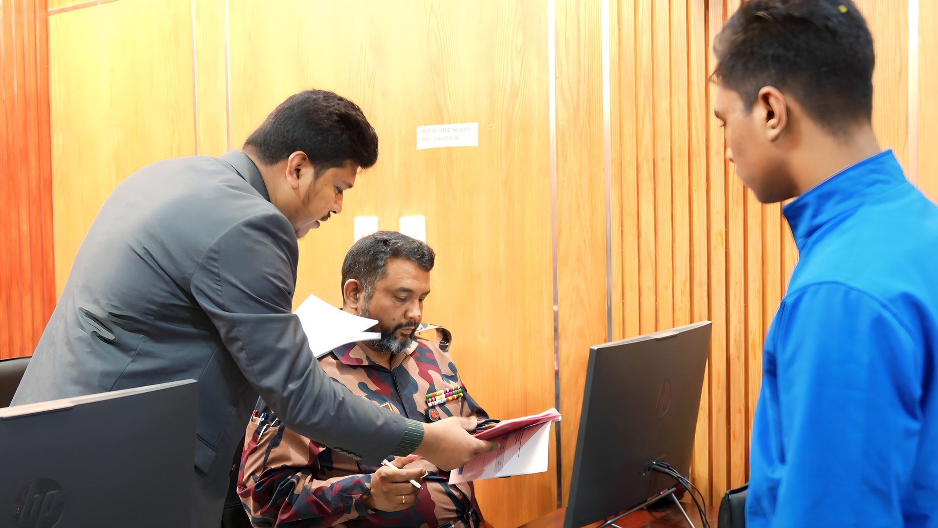 Raihan Khan reviews training documents with a uniformed officer at a computer workstation in the IMED office.