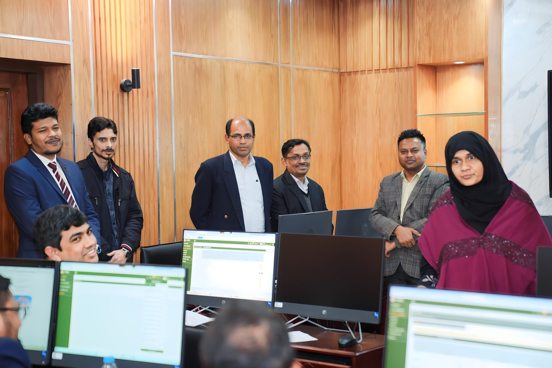 The project team poses for a photo behind a row of computer screens displaying the e-PMIS application.