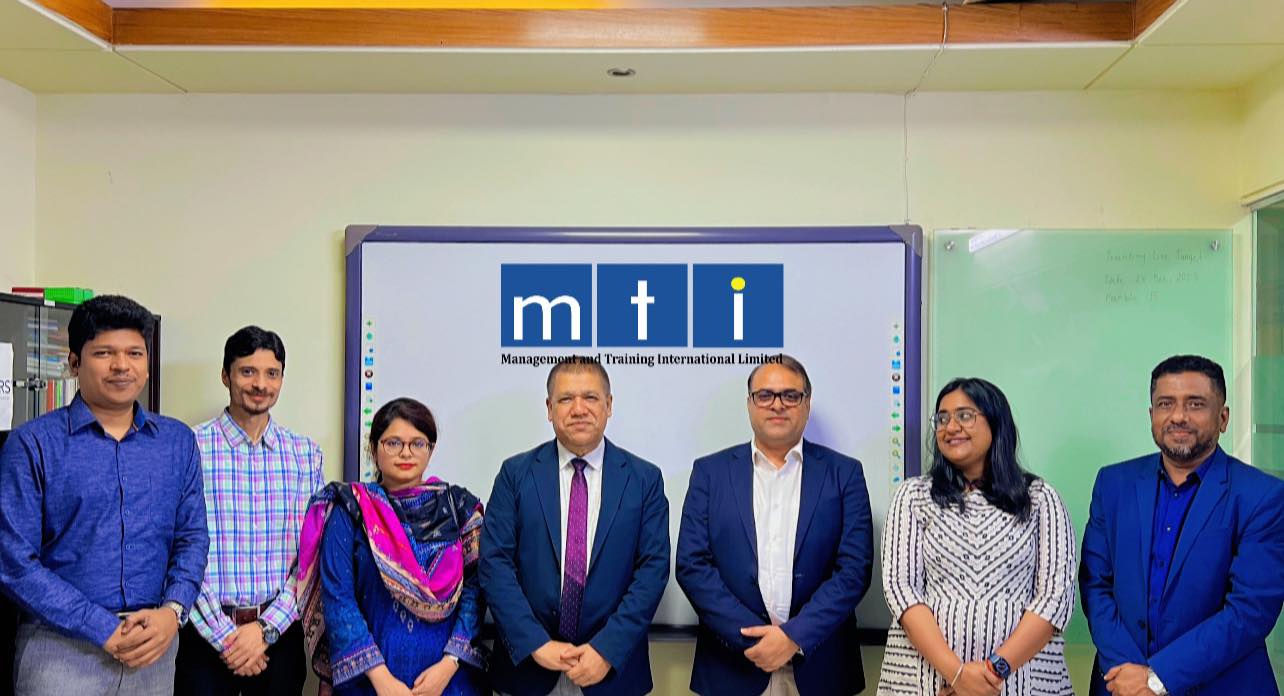Raihan Khan poses with MTI Ltd. colleagues in front of a branded training room screen.