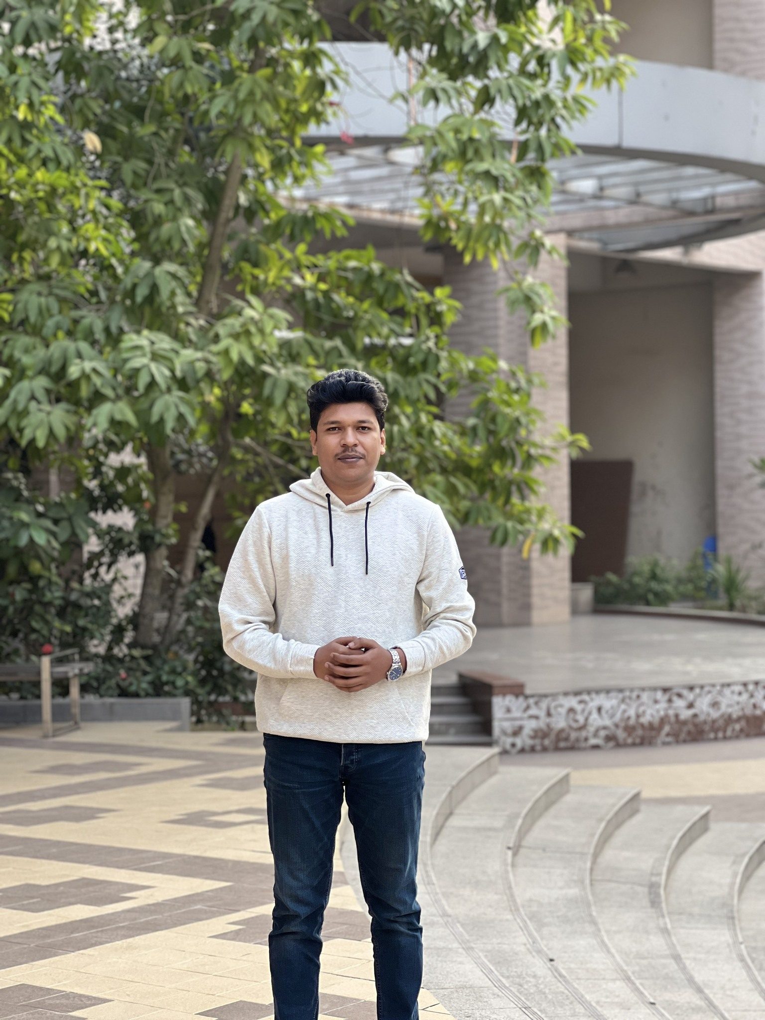 Raihan Khan in a cream hoodie standing near the amphitheater steps on campus.