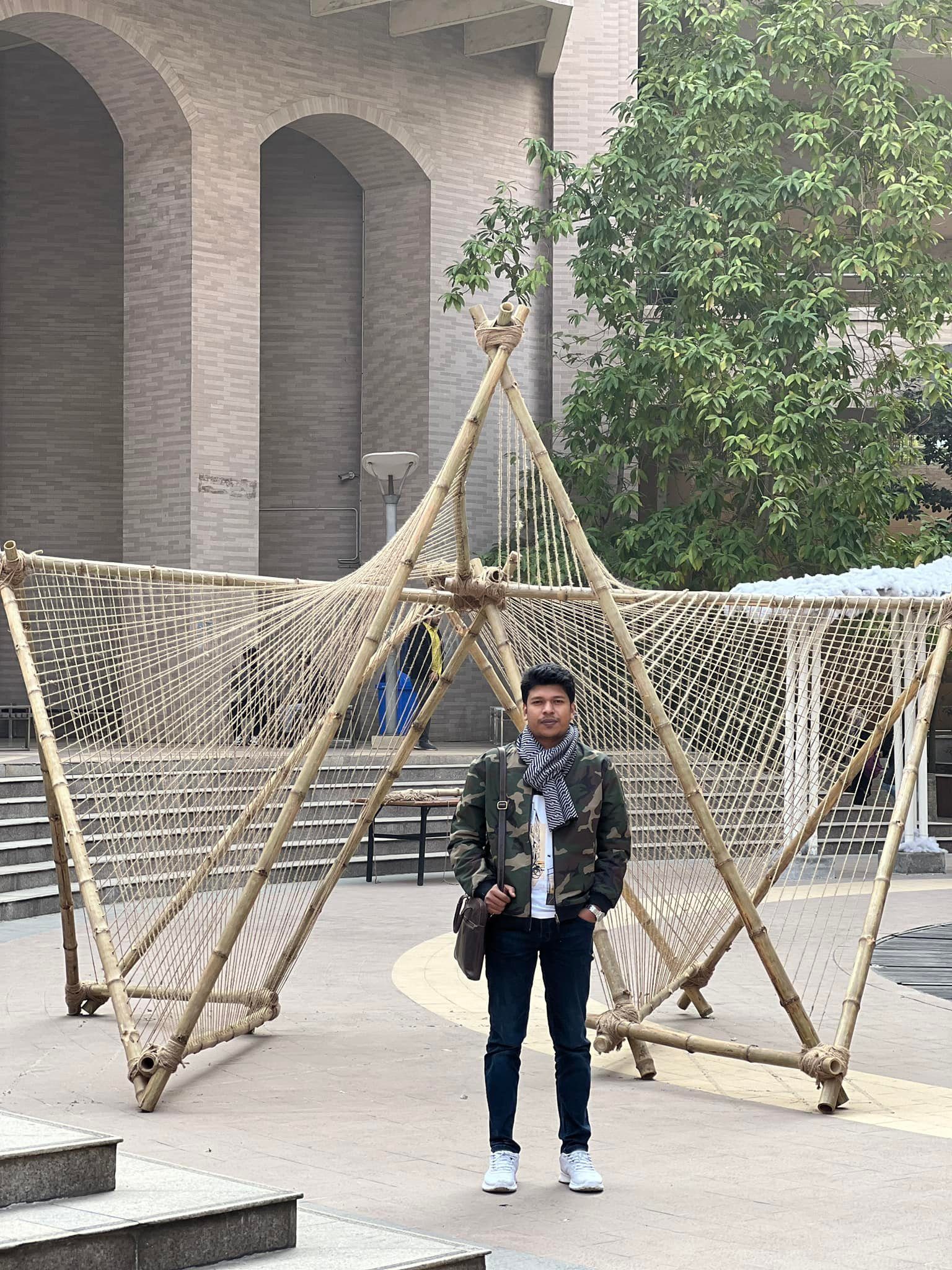 Raihan Khan standing beneath a large bamboo and rope art installation in the NSU campus plaza.