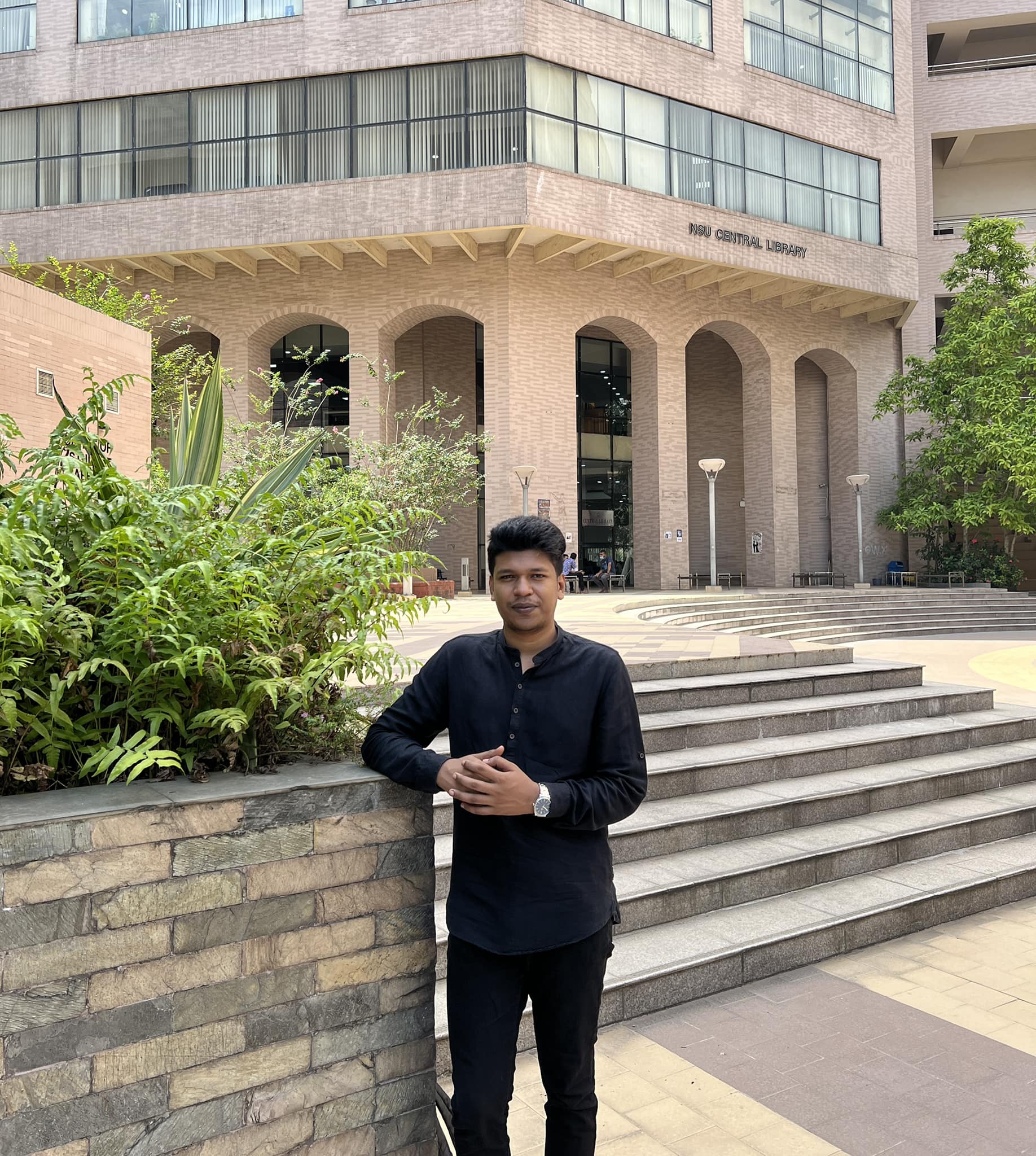 Raihan Khan in a black kurta leaning against a stone wall outside the NSU Central Library.