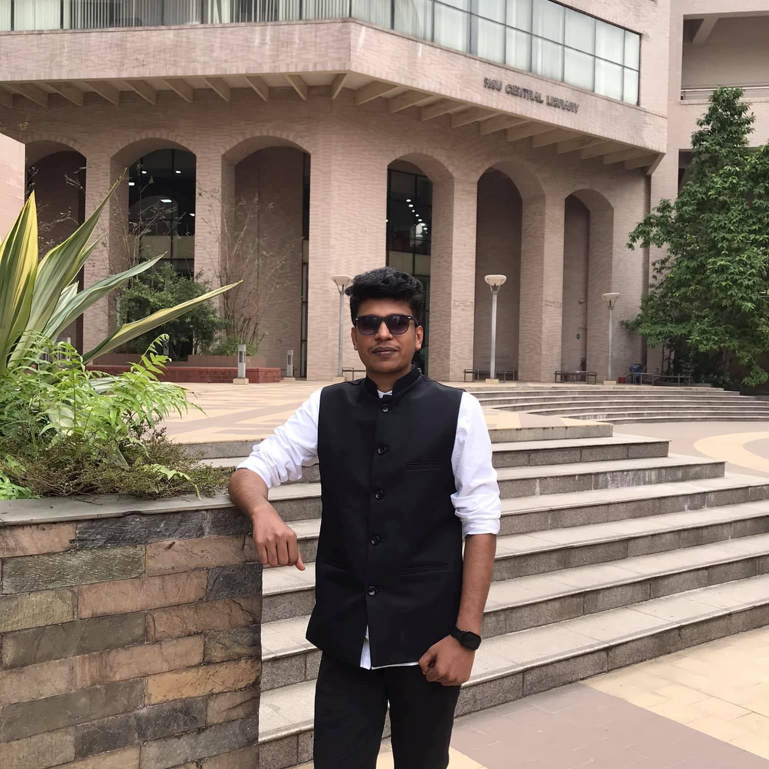 Raihan Khan wearing sunglasses and a black waistcoat outside the NSU Central Library entrance.