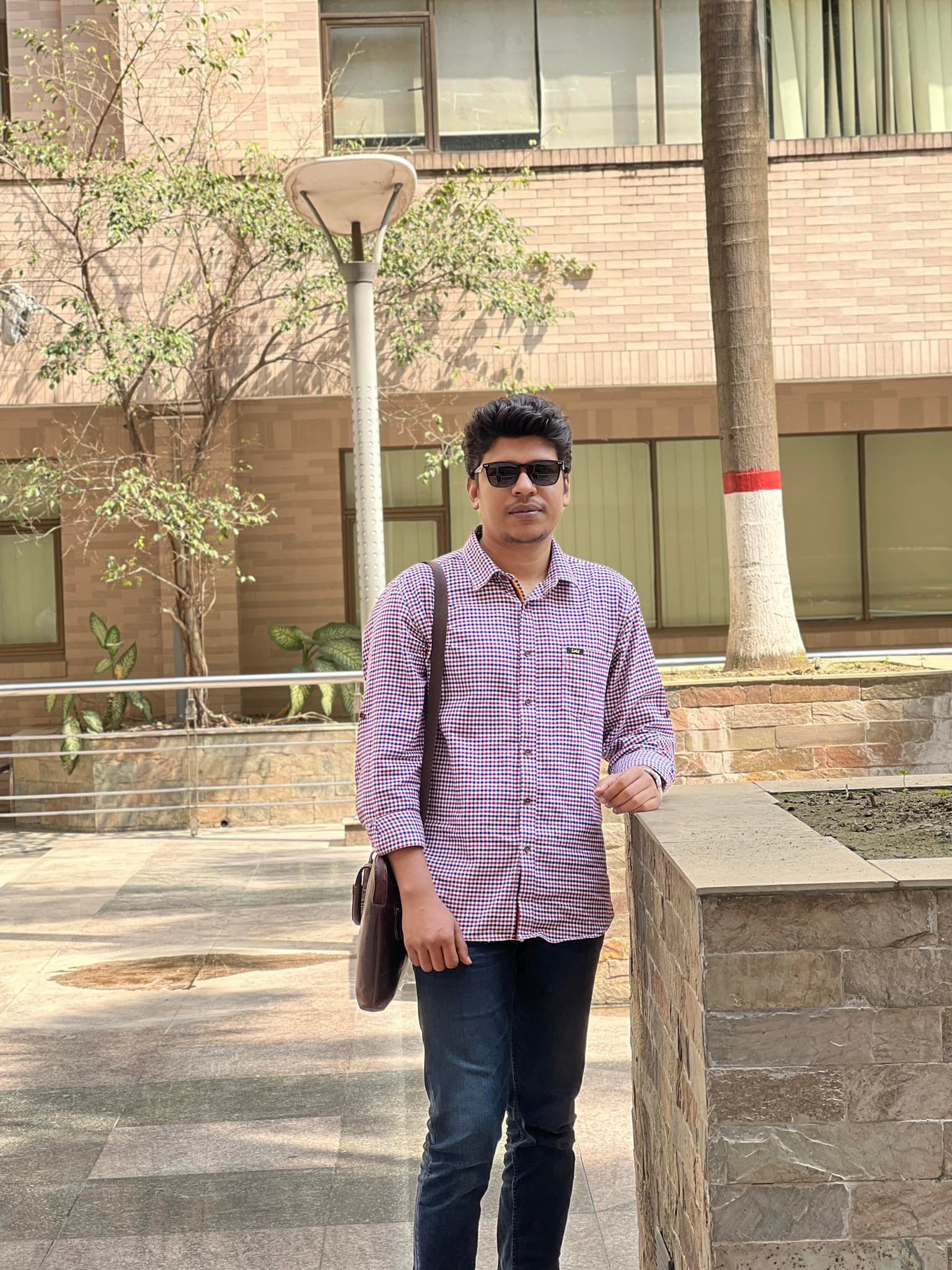 Raihan Khan in a checkered shirt and sunglasses standing beside a painted palm tree trunk.
