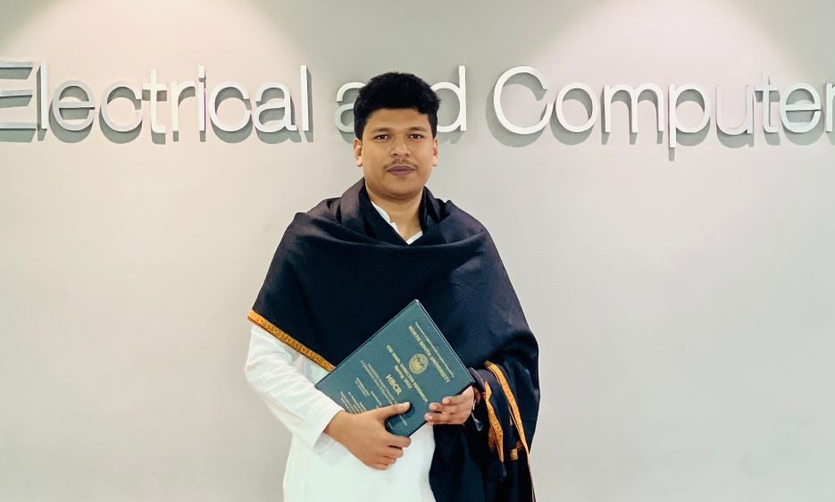 Raihan Khan holding his North South University certificate beside the Electrical and Computer Engineering department sign.