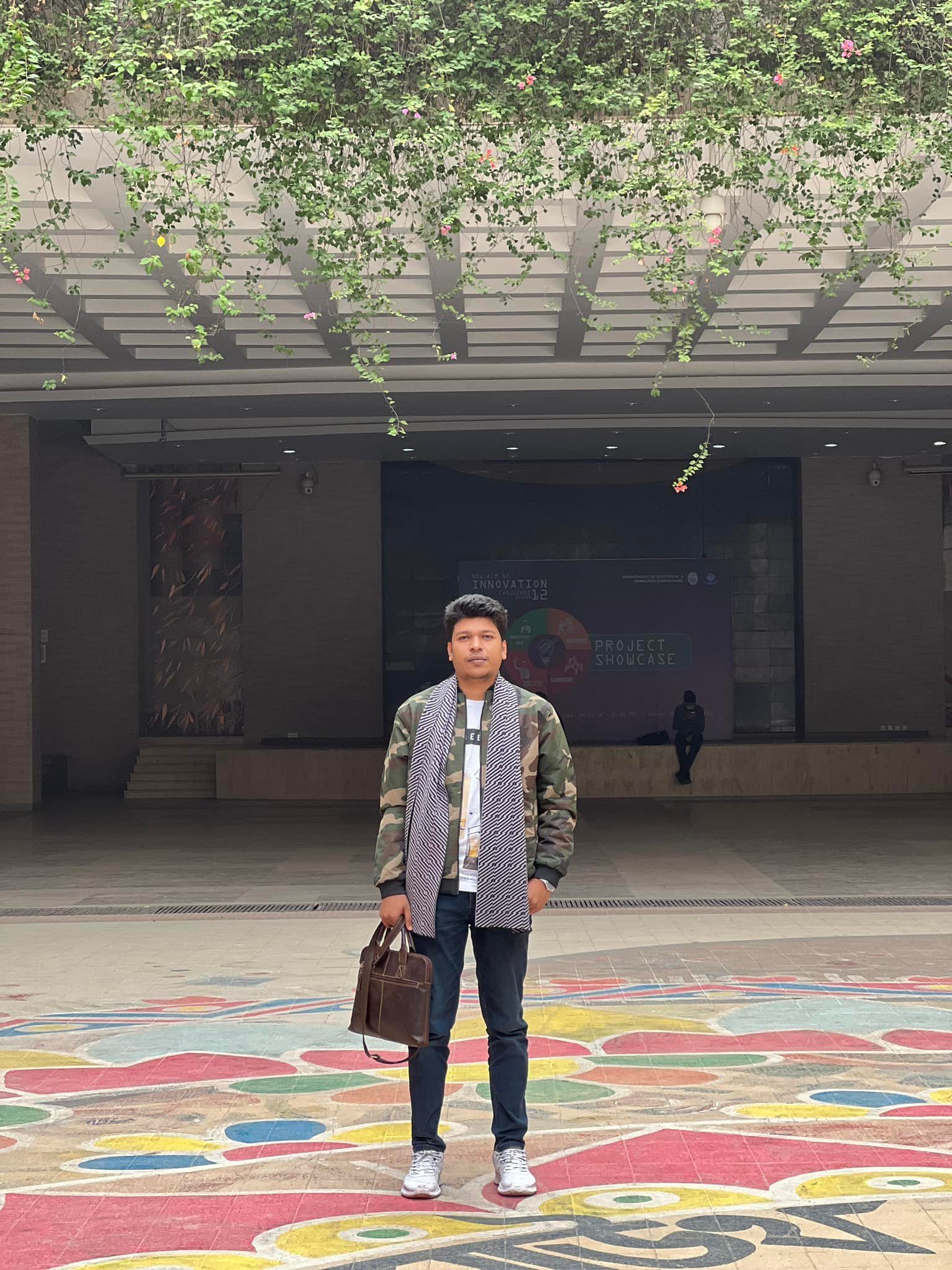 Raihan Khan standing on a colorful mandala floor mural at the NSU Innovation Challenge project showcase.
