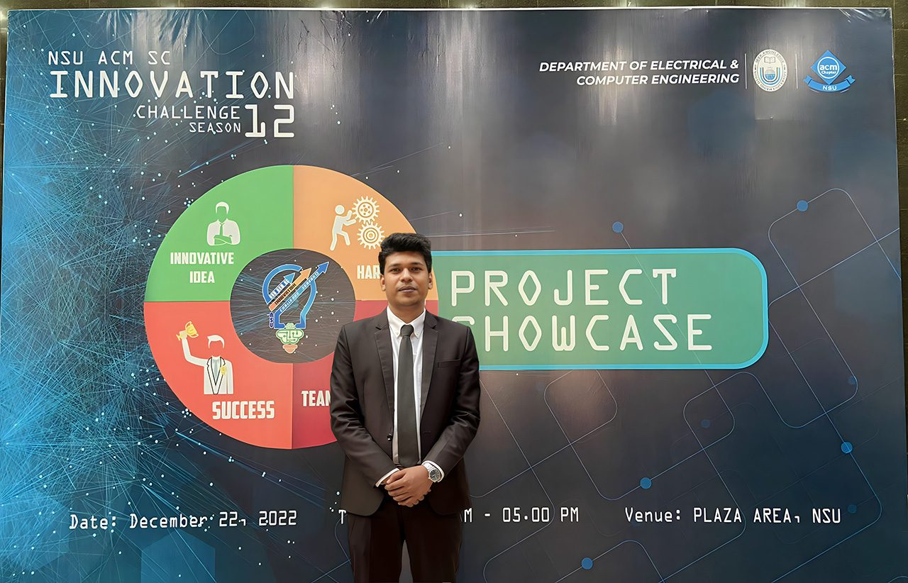 Raihan Khan in a suit standing before the NSU ACM Innovation Challenge Season 12 showcase banner.