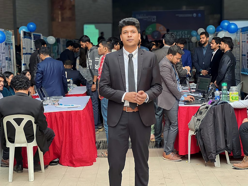 Raihan Khan in a suit and tie walking through the crowd at the NSU project showcase event.