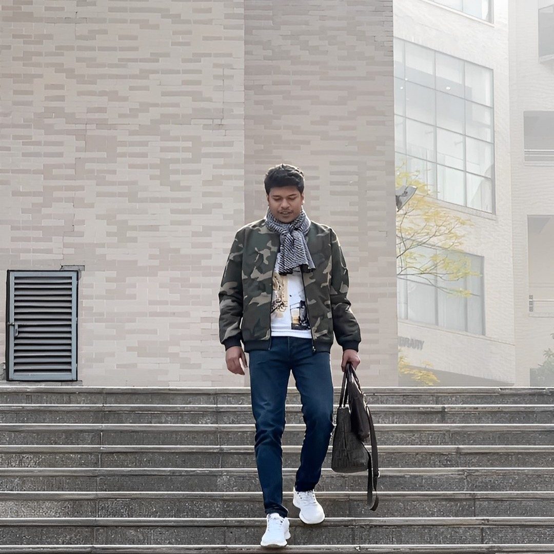 Raihan Khan walking down an outdoor staircase on campus carrying a leather bag.