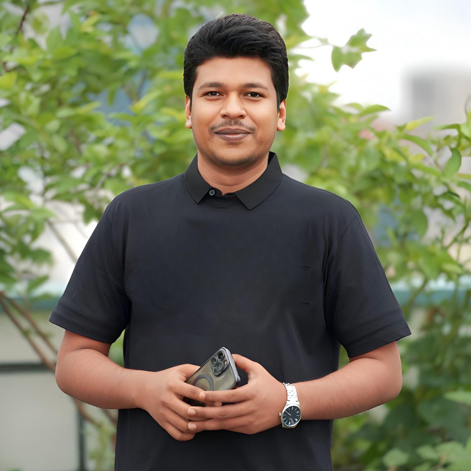 Raihan Khan in a black polo shirt holding his phone while standing among rooftop garden greenery.