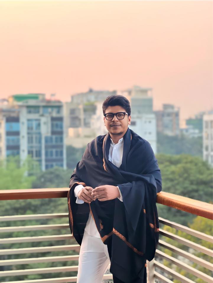 Raihan Khan in a white kurta draped with a black embroidered shawl on a rooftop at dusk.
