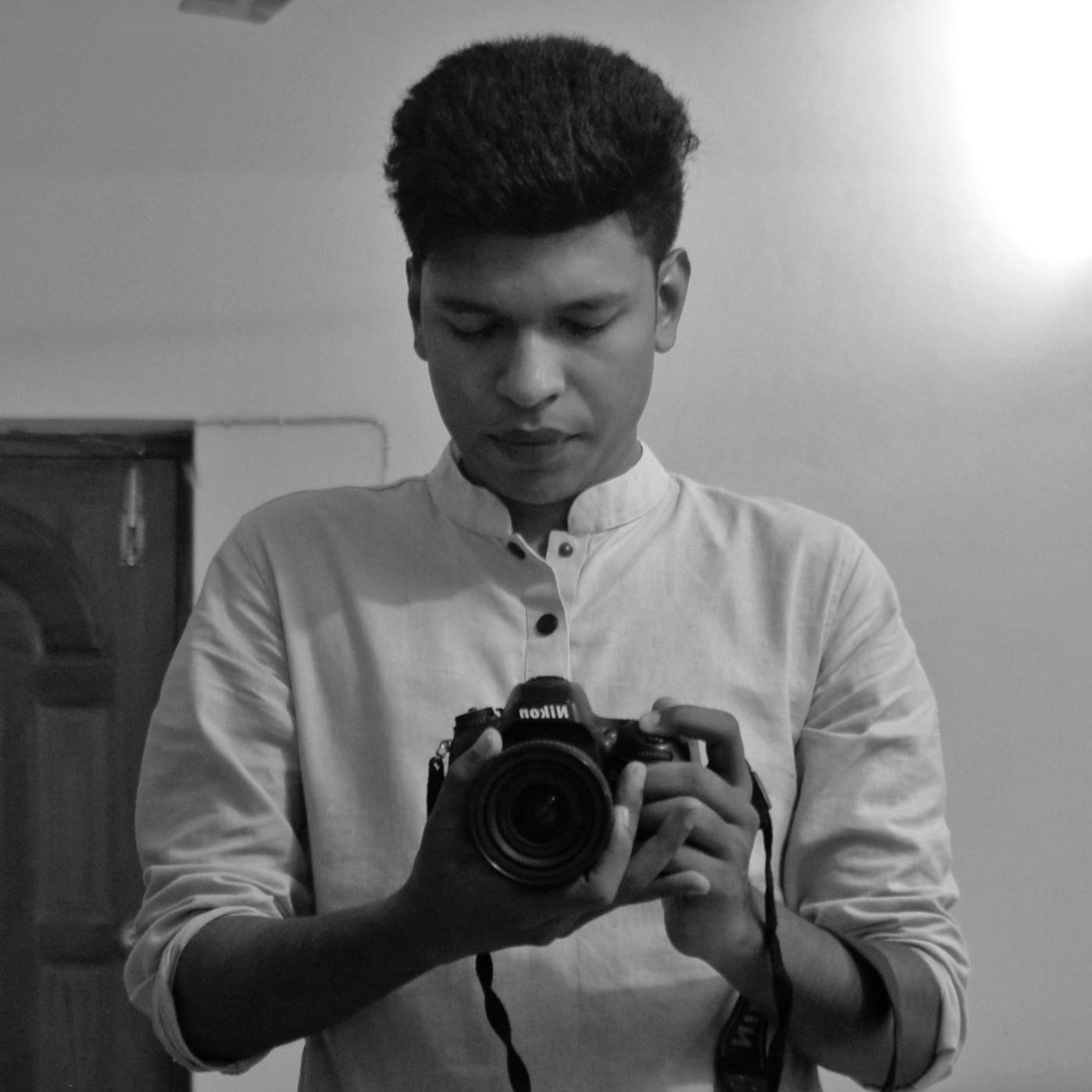 A black and white photo of Raihan Khan in a white kurta holding a Nikon DSLR camera.