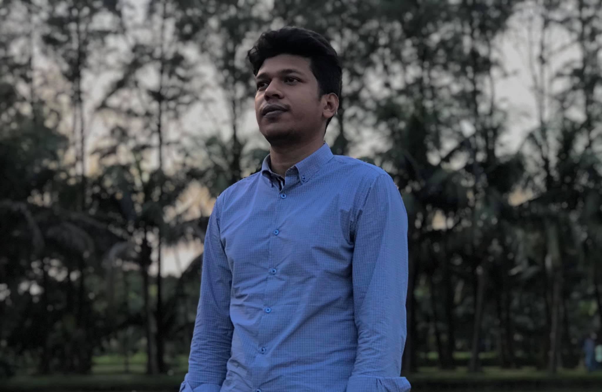 Raihan Khan in a light blue checkered shirt gazing off to the side in a park at dusk.