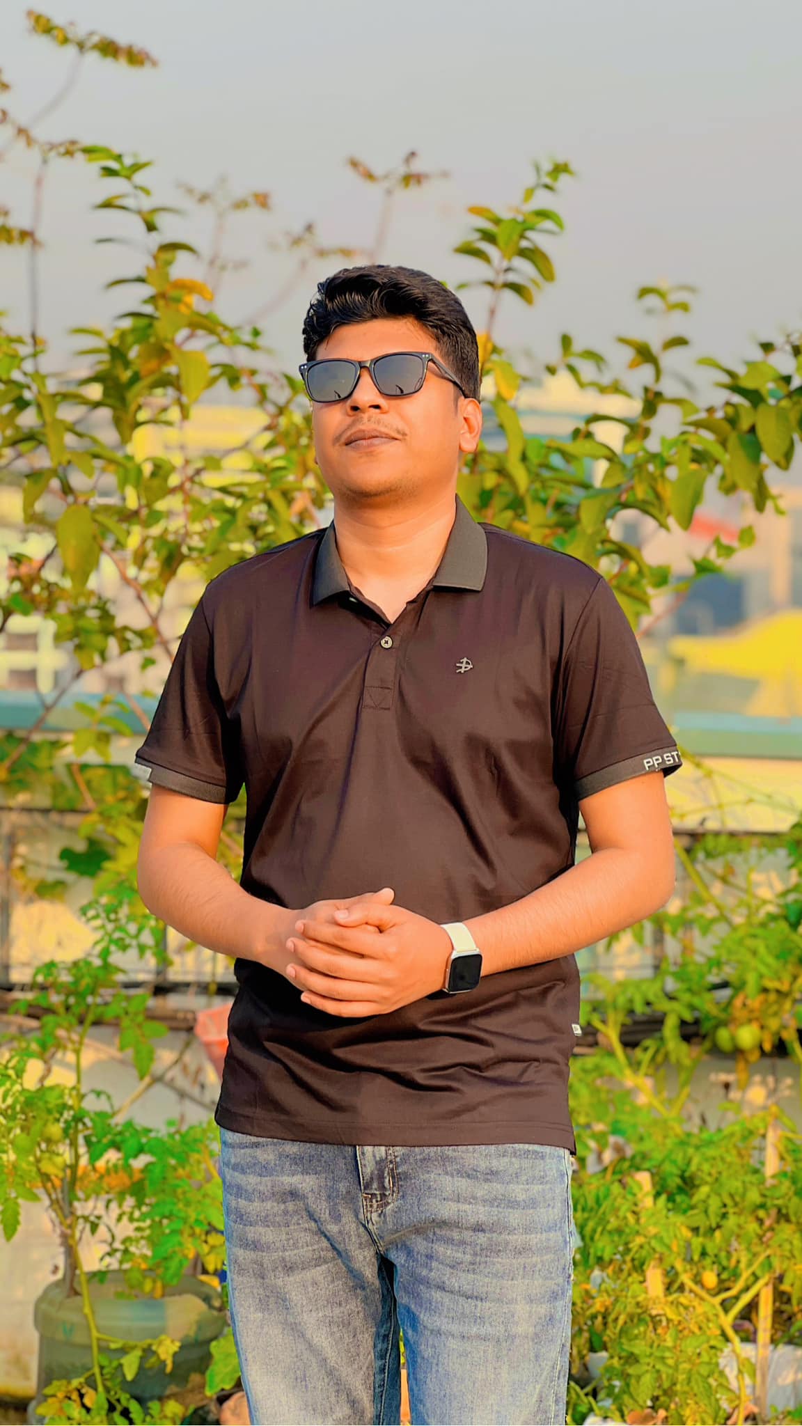 Raihan Khan in a brown polo shirt with sunglasses looking upward on a rooftop surrounded by greenery.