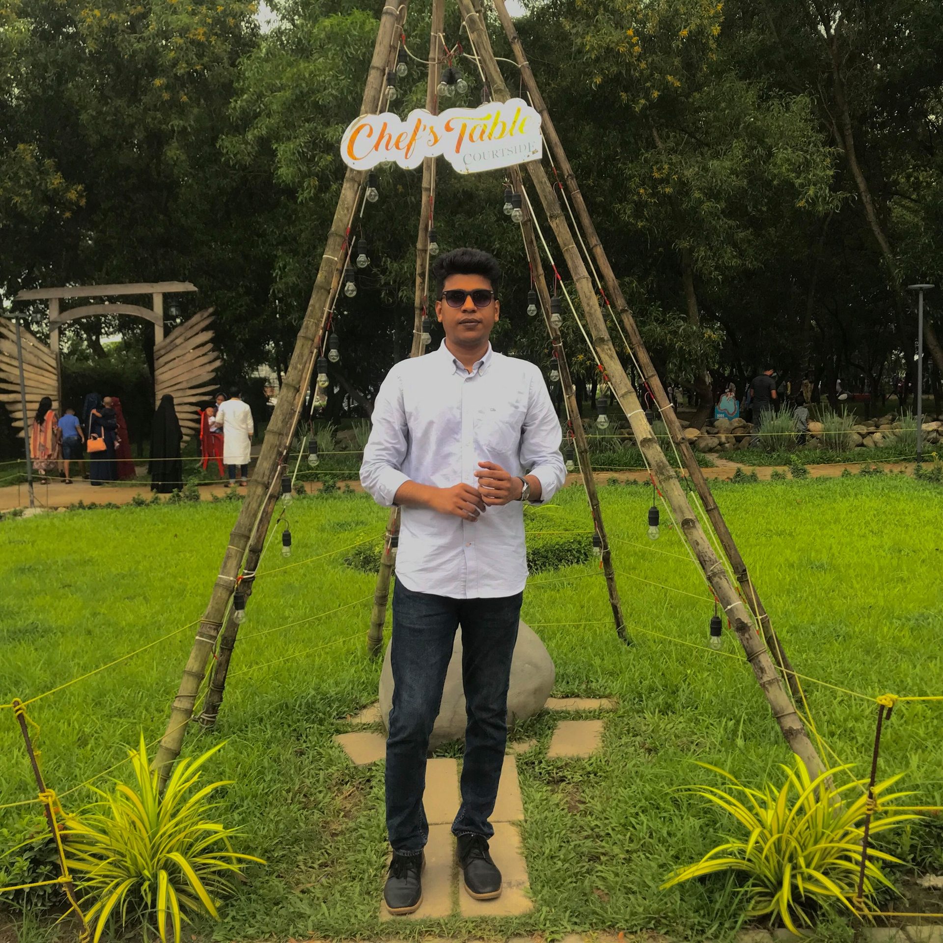 Raihan Khan in a white shirt standing beneath a bamboo teepee structure under a Chef's Table sign in a park.