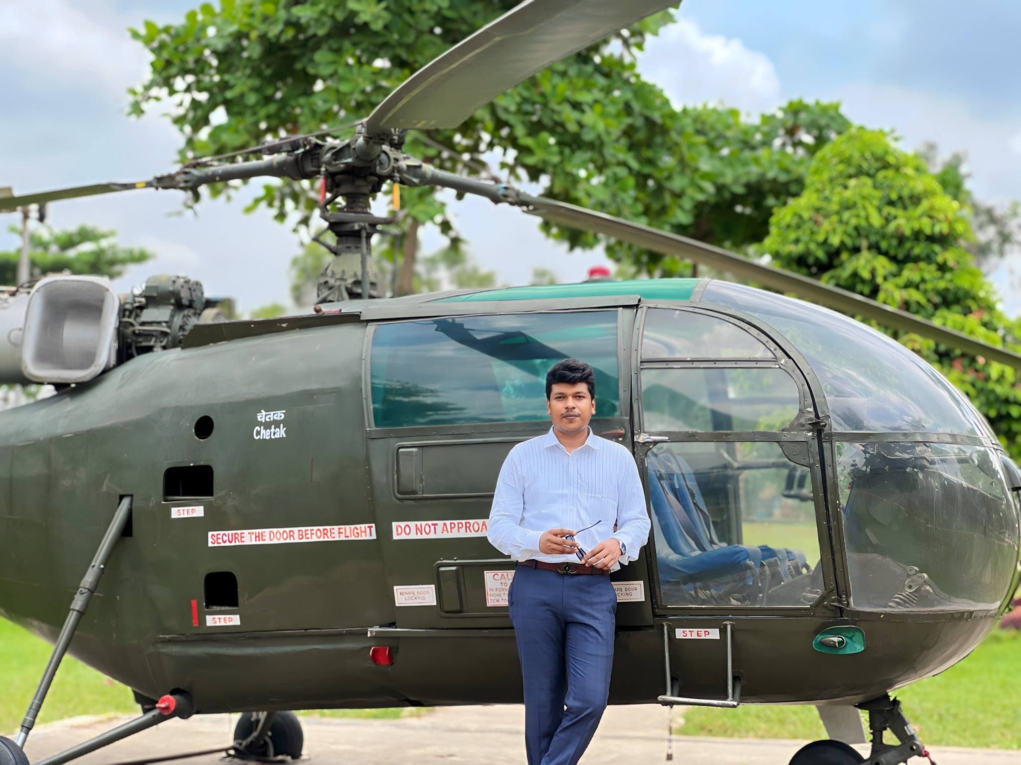 Raihan Khan in a white striped shirt standing in front of a retired military Chetak helicopter on display.
