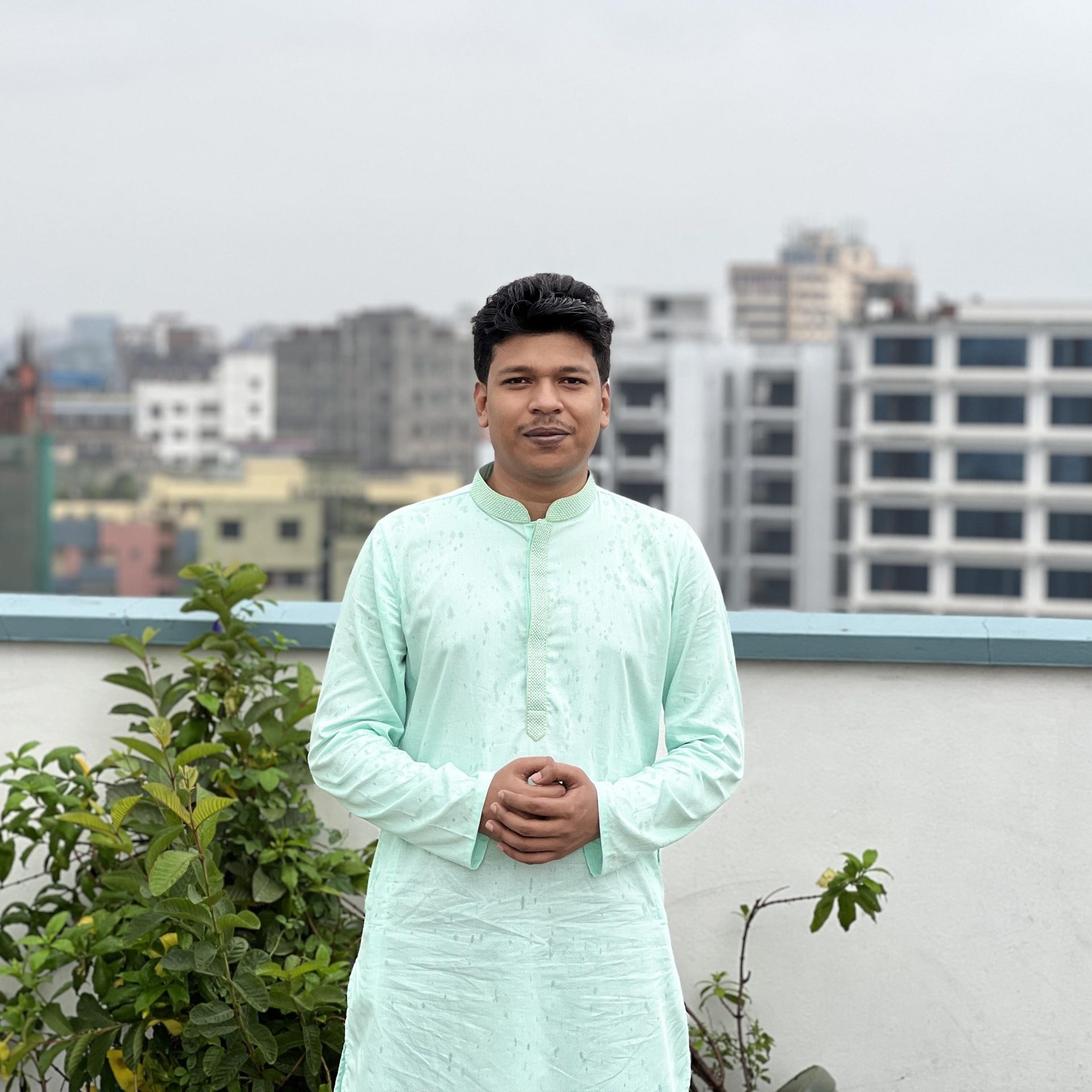 Raihan Khan in a mint green embroidered kurta standing on a rooftop with the city skyline in the background.