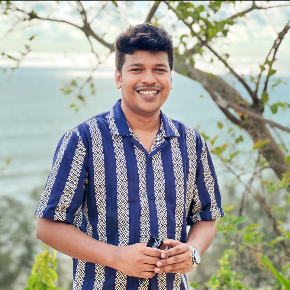 Raihan Khan in a navy striped shirt laughing broadly on a beach with the sea in the background.