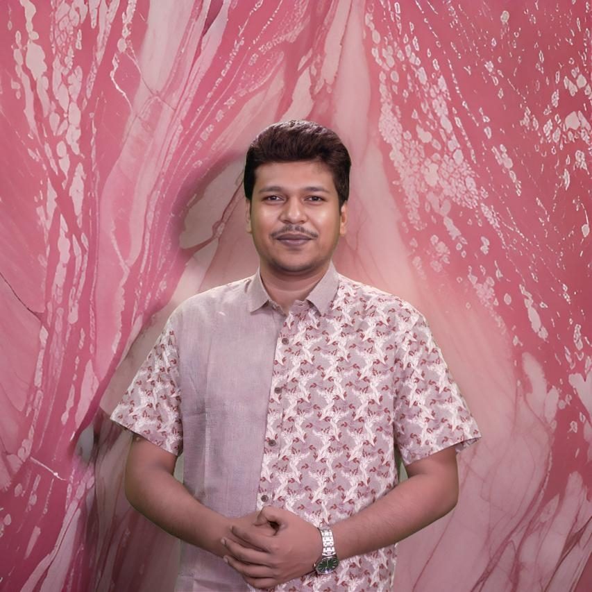 Raihan Khan in a patterned pink shirt posing against a pink marble-effect studio backdrop.