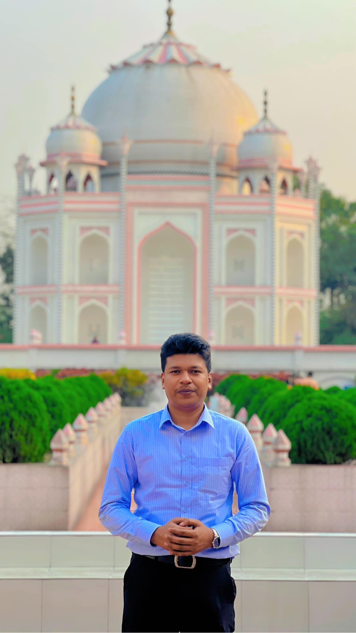 Raihan Khan in a blue striped shirt standing before an ornate domed monument resembling the Taj Mahal.
