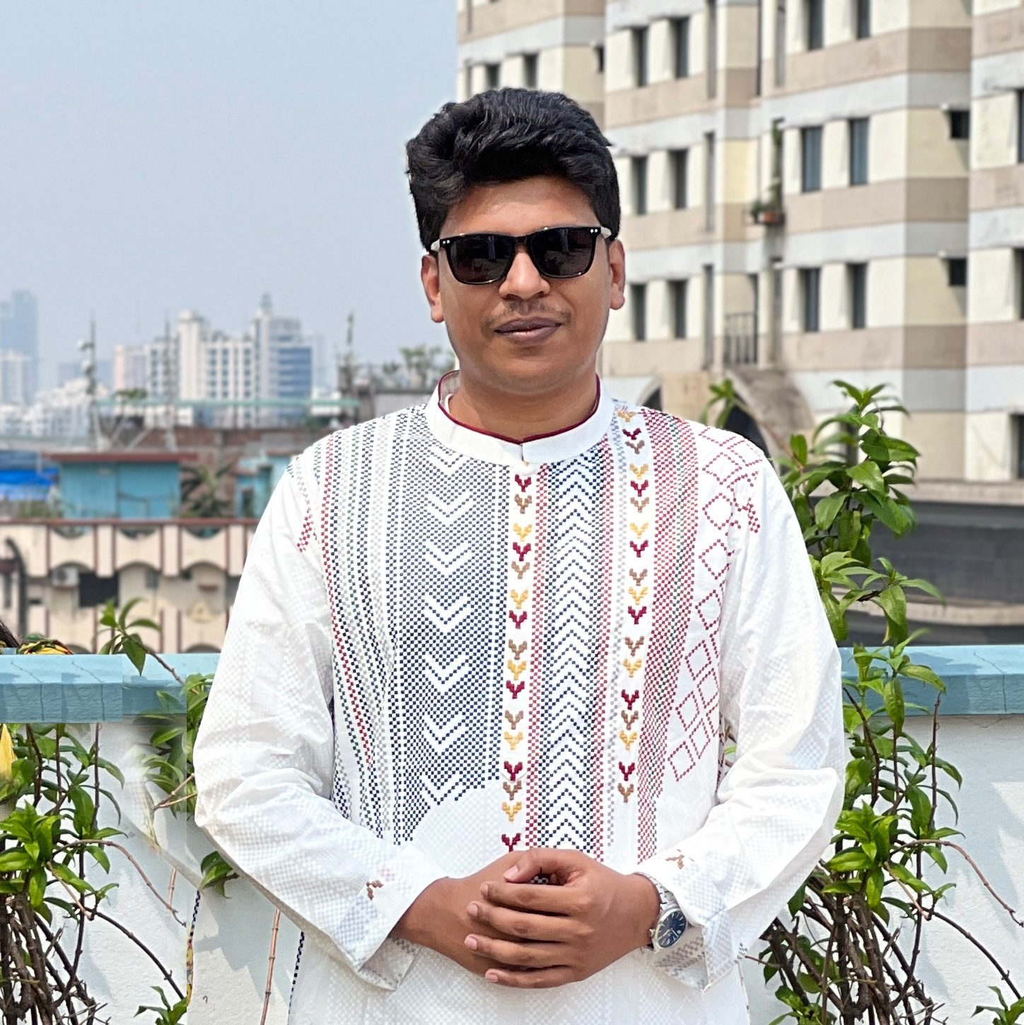 Raihan Khan in a white embroidered kurta with sunglasses standing on a rooftop overlooking the city skyline.