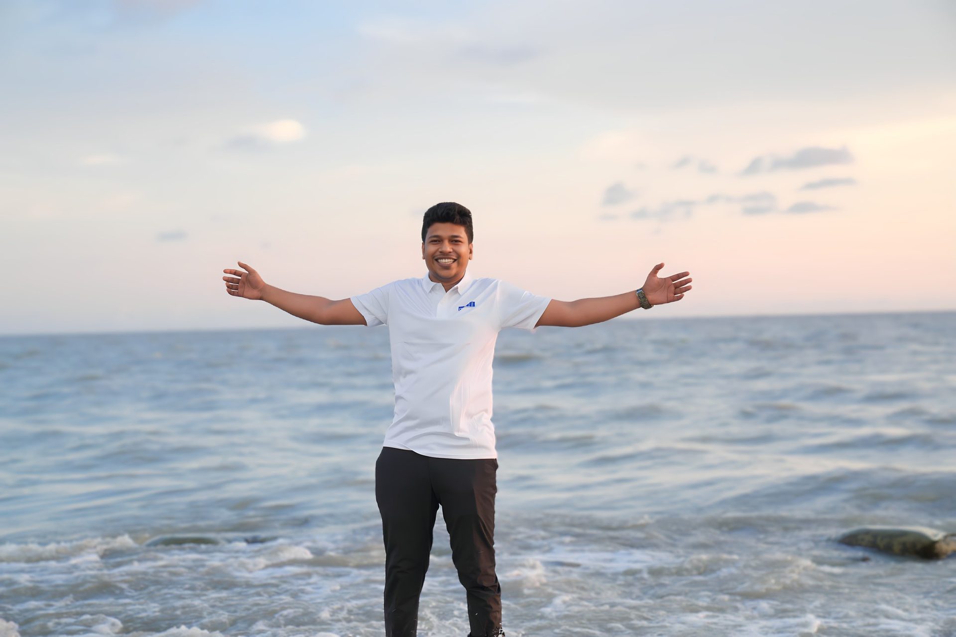 Raihan Khan spreading his arms wide on the beach as the sun sets over the sea.