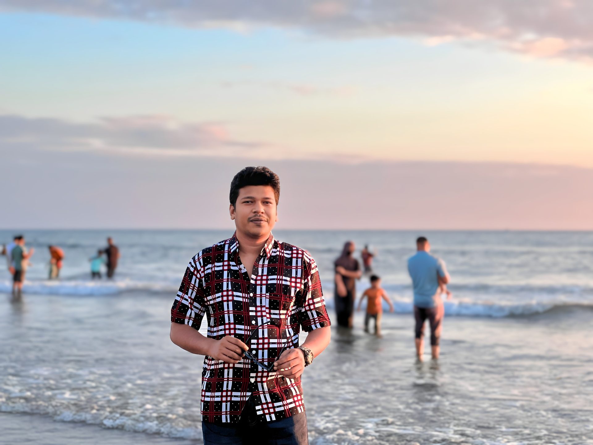 Raihan Khan on the beach at sunset while families wade in the waves behind him.