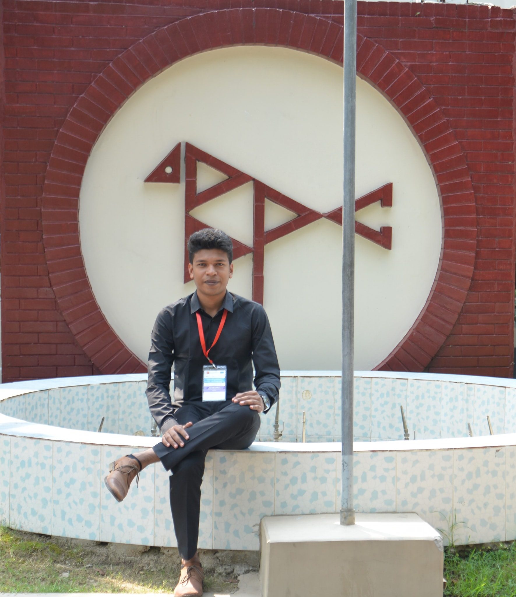 Raihan Khan sitting by a decorative circular wall emblem in a courtyard fountain area.