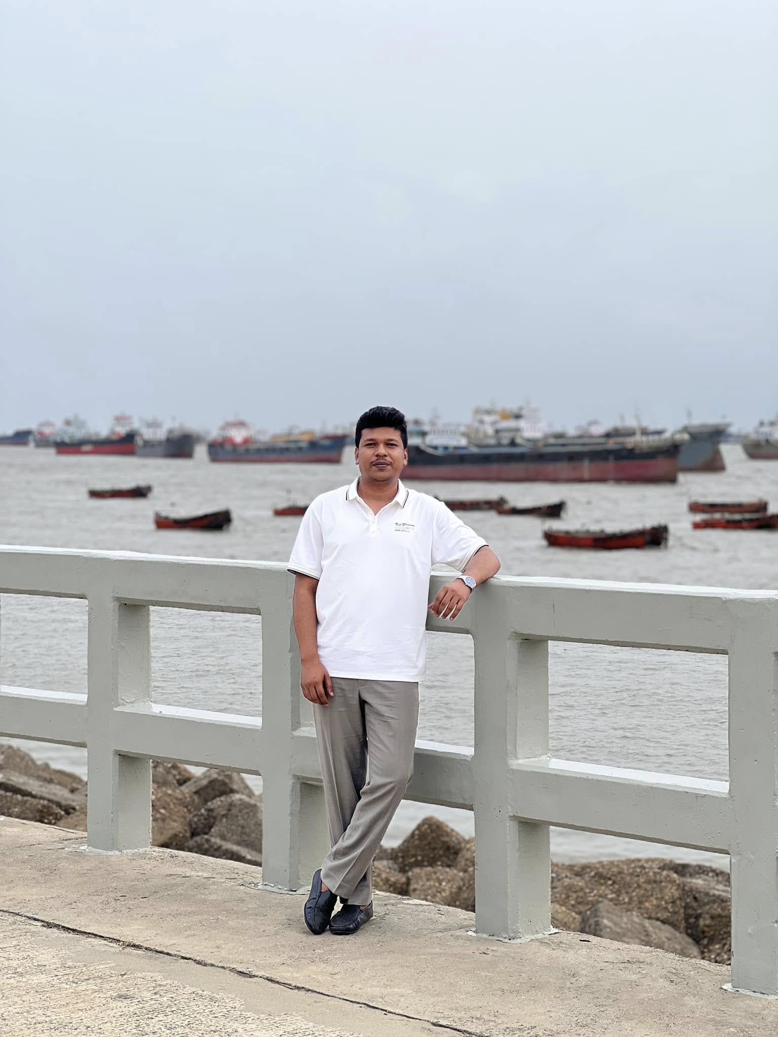 Raihan Khan leaning on a pier railing overlooking anchored ships and fishing boats.