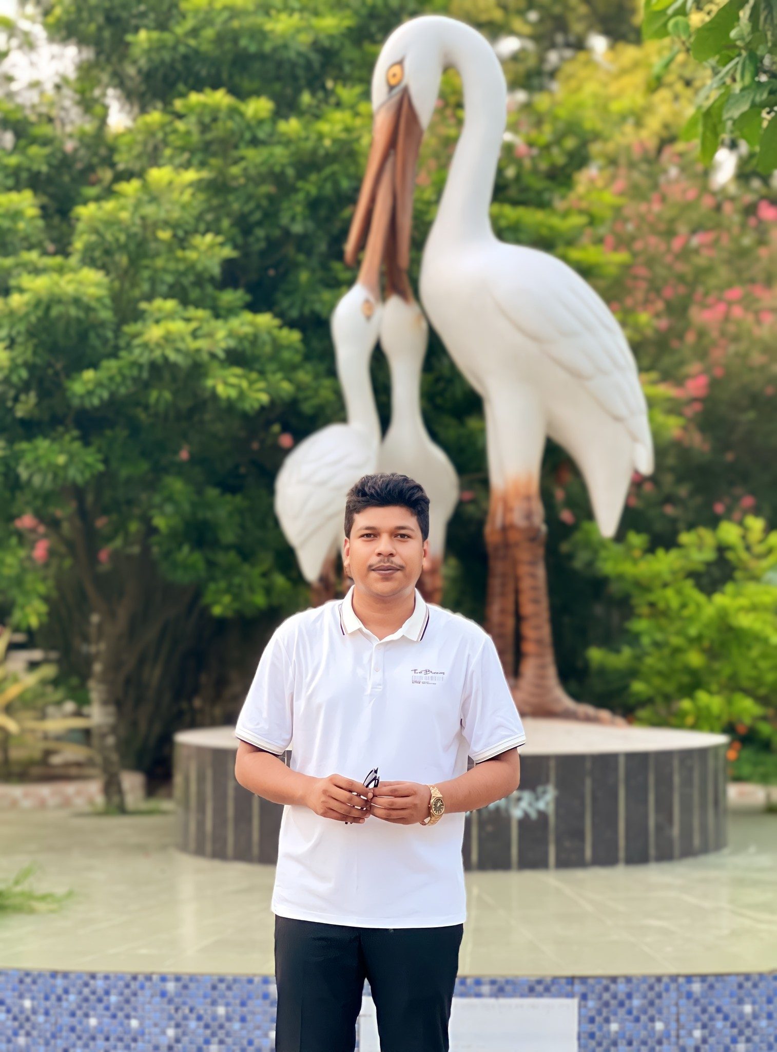 Raihan Khan standing in front of tall white pelican-like bird statues in a park.