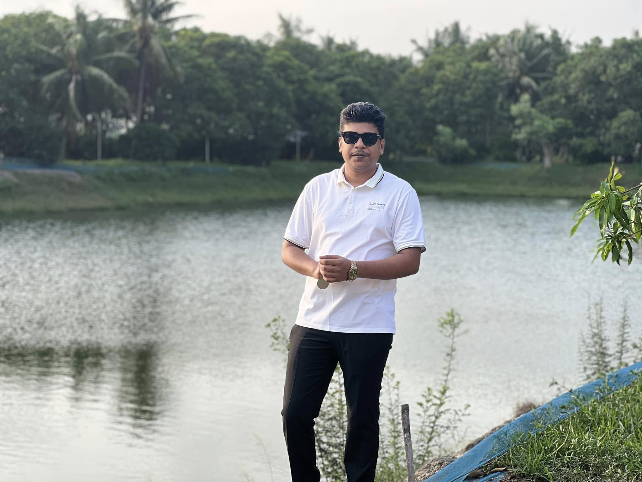 Raihan Khan walking along a pond bank lined with coconut palms and mango trees.
