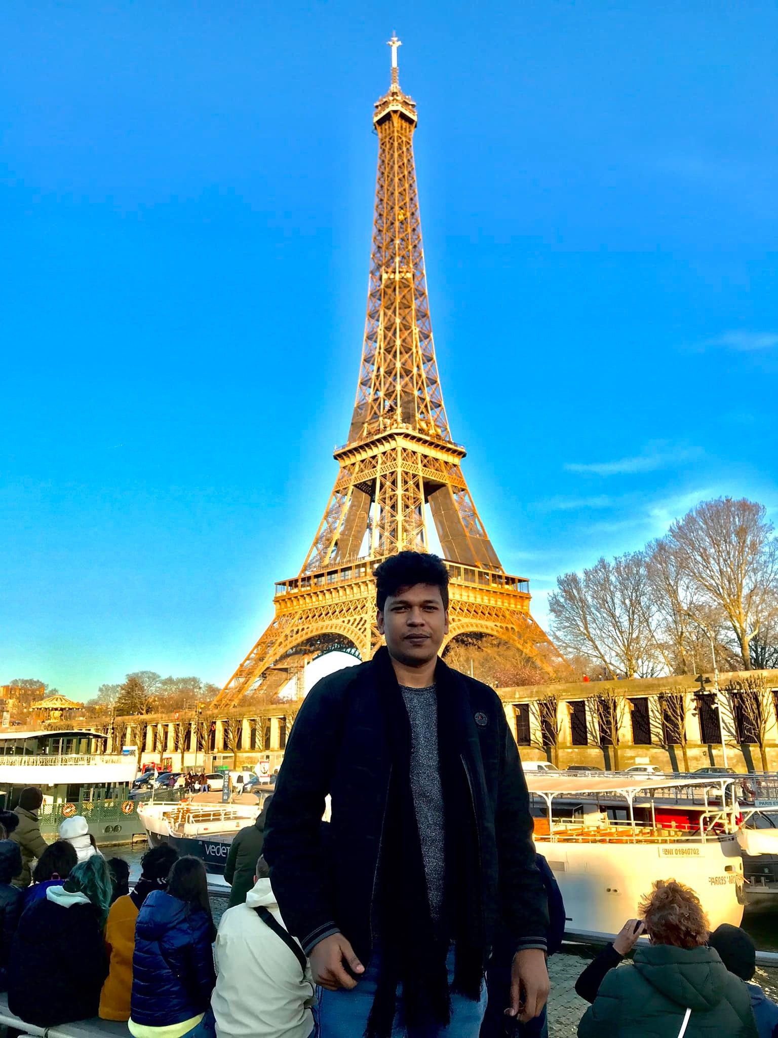 Raihan Khan posing beside the Eiffel Tower in Paris as it glows gold at sunset.