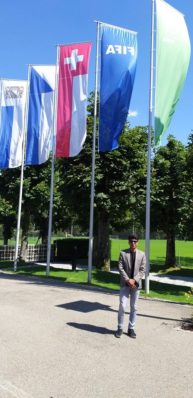 Raihan Khan standing beneath a row of national and FIFA flags at FIFA headquarters in Zurich.