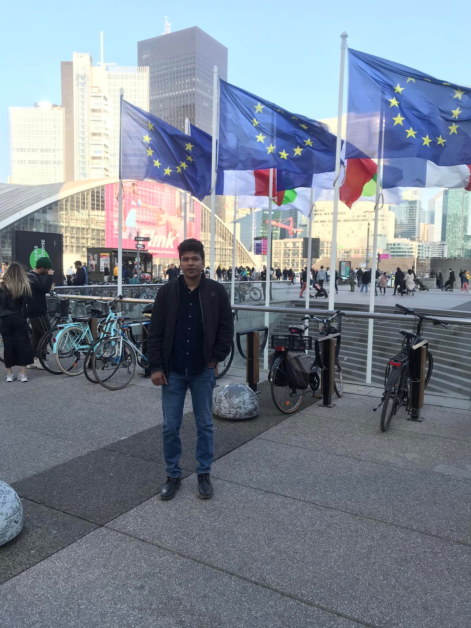 Raihan Khan standing among European Union flags in the La Défense business district of Paris.