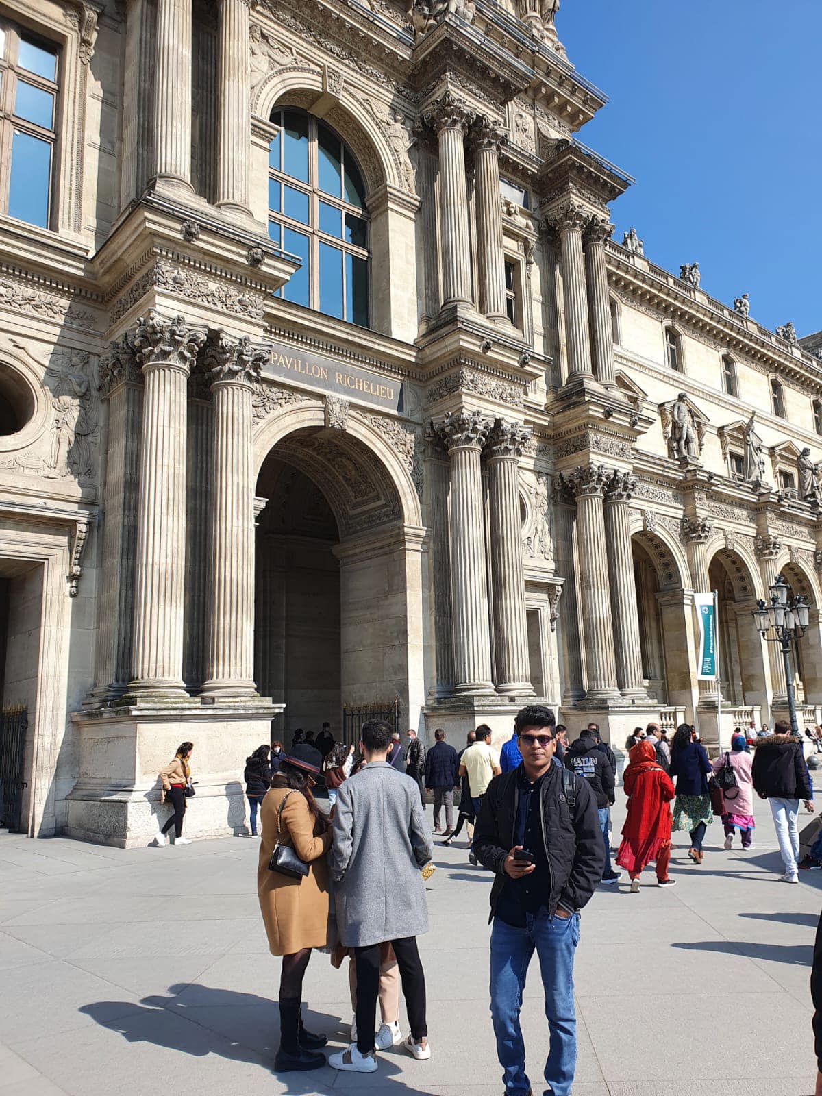 Raihan Khan standing outside the Pavillon Richelieu facade of the Louvre Museum in Paris.