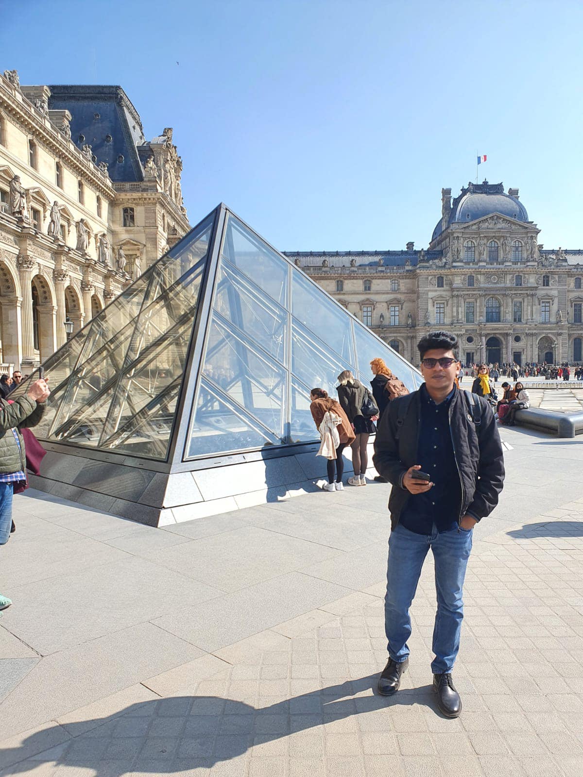 Raihan Khan standing near the glass pyramid outside the Louvre Museum in Paris.