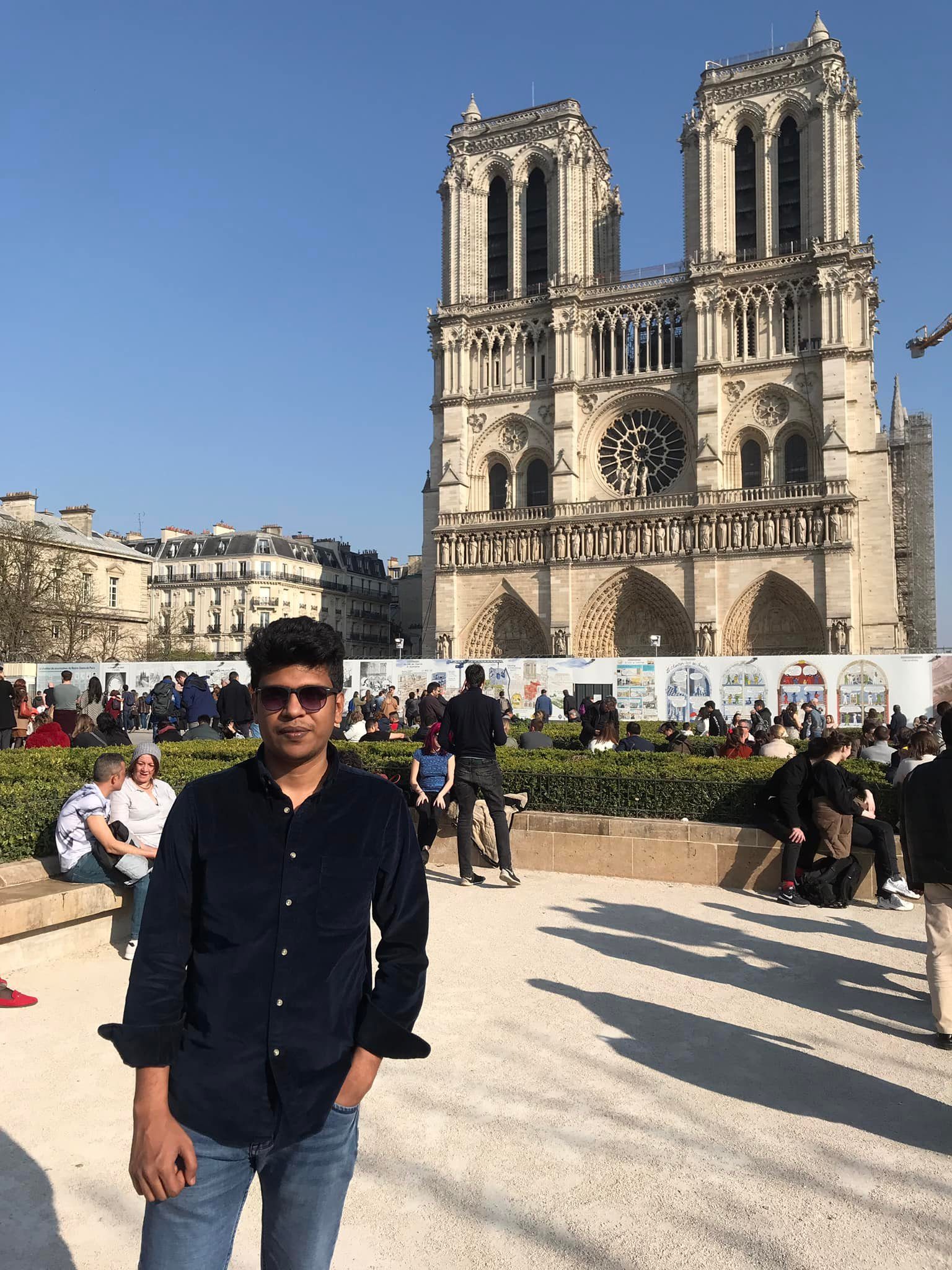 Raihan Khan standing alone in front of the twin towers of Notre-Dame Cathedral in Paris.