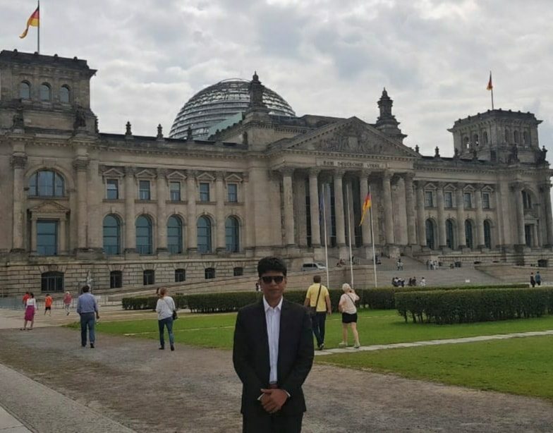 Raihan Khan standing on the plaza in front of the Reichstag building and its glass dome in Berlin.