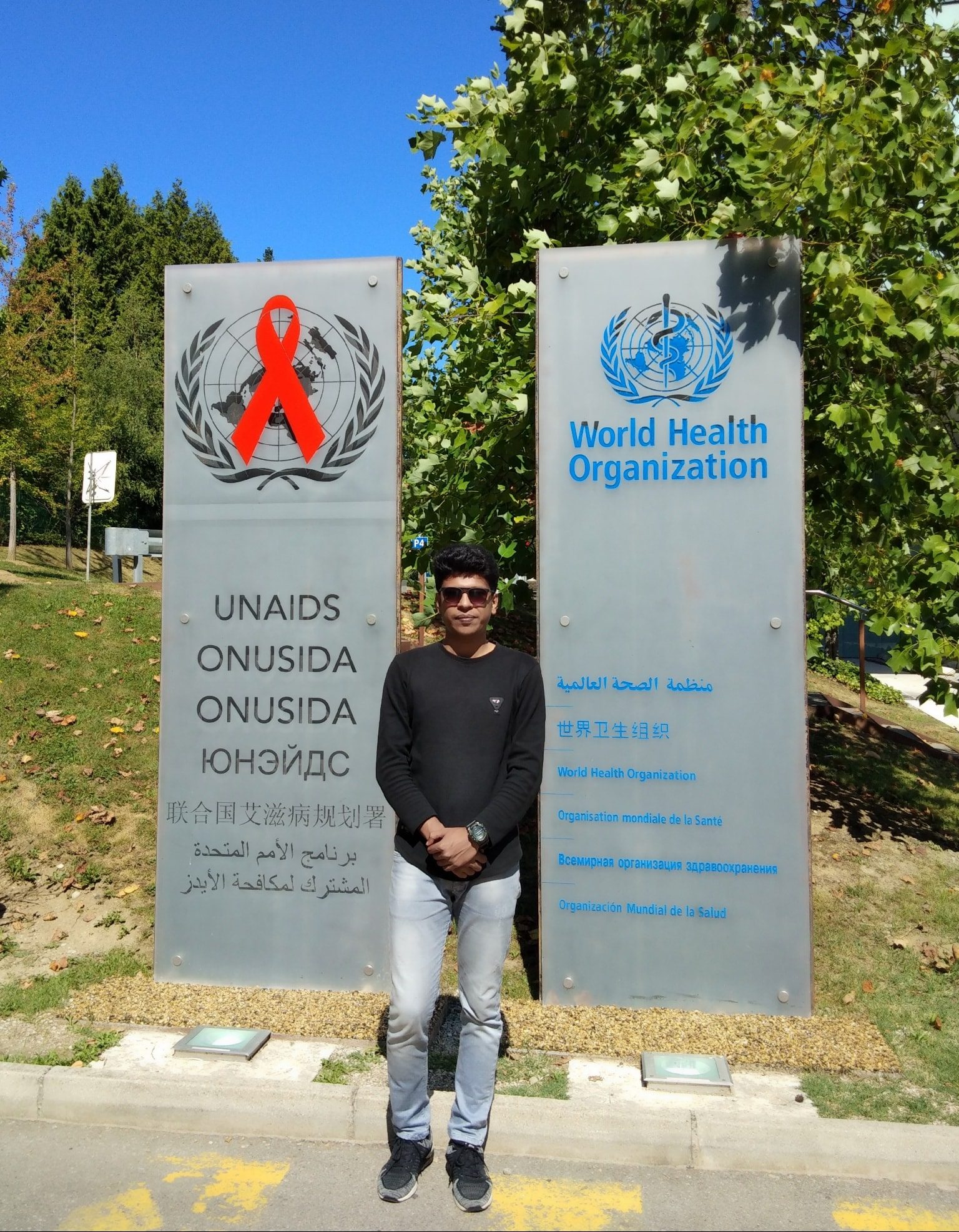 Raihan Khan standing between the UNAIDS and World Health Organization signs in Geneva.