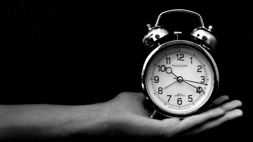 A hand holding an alarm clock, in black and white